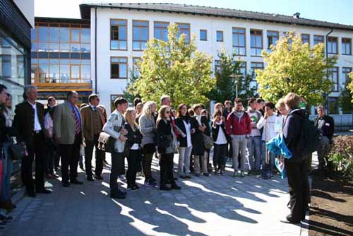 Viele Personen stehen vor und neben dem Gebäude des Rottmayr-Gymnasiums zwischen Bäumen.