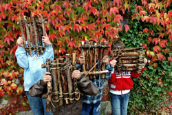 Vier Kinder stehen vor einer herbstlichen mit wildem Wein begrünten Wand und halten sich selbstgemachte Holzflöße vor die Gesichter.