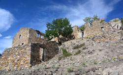 Aus Bruchsteinen gemauerte Häuserreste eines verlassenen Dorfes auf kahlem Boden mit einem einzigen grünen Baum in der Mitte.