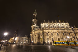Nachtaufnahme der flächig beleuchteten Dresdner Hofkirche mit Straßenbahn davor.