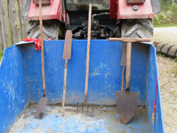 Das Foto zeigt die blaue Ladefläche eines Traktors mit verschiedenen Torfstichwerkzeugen.