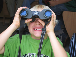 Ein Junge mit Zahnlücken hält ein Fernglas in den Händen und sieht sich etwas aus der Ferne an.