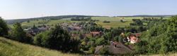 Panoramabild einer Landschaft mit Siedlung, Feldern und Wäldern.