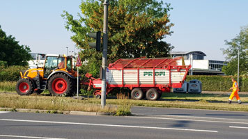 Ein Traktor mit Anhänger nimmt am Straßenrand Mahdgut auf.