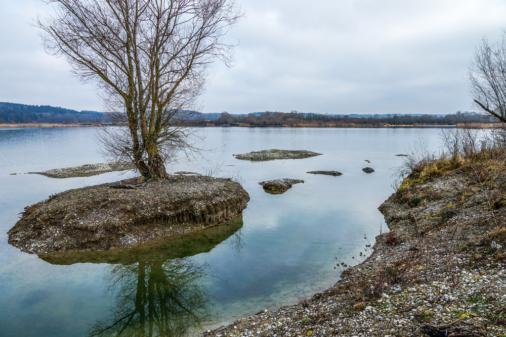 Blick über einen See mit kleiner baumbestandener Insel.