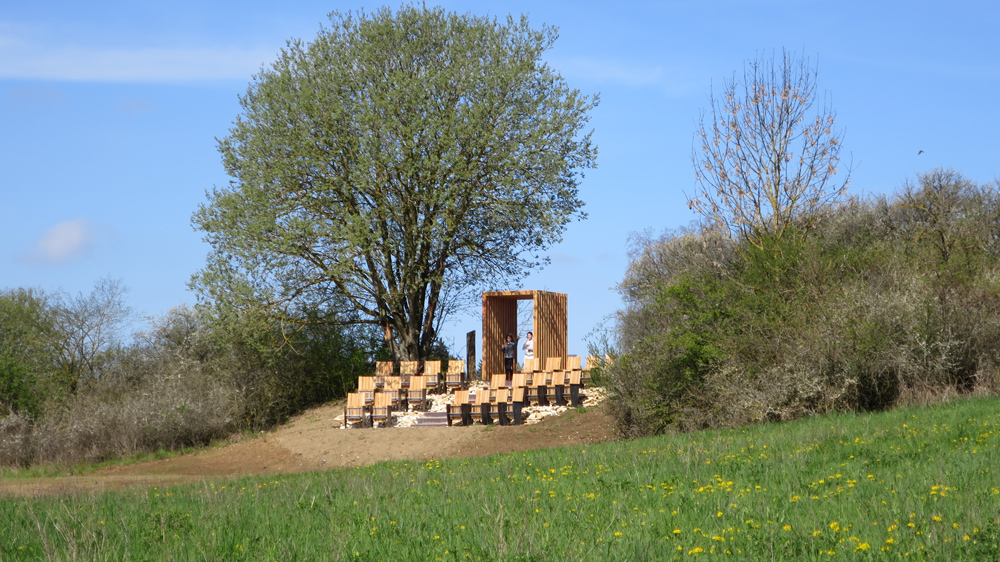 Zwei Dutzend Klappstühle aus Holz stehen in der freien Landschaft und bilden ein Open-Air-Kino der besonderen Art.