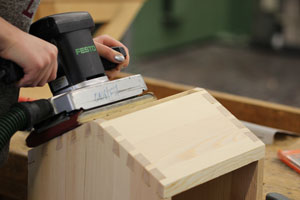 Ein Holzkasten, der später von Hornissen genutzt werden soll, wird mit einer Schleifmaschine bearbeitet.