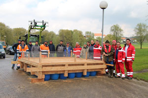 Ein Gruppe Männer steht um ein neu gebautes, großes Floß, das auf der Straße abgestellt ist. Im Hintergrund sieht man einen Traktor mit Gabelstapler.