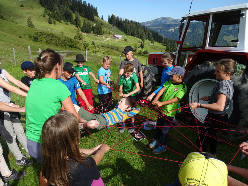 Ein Junge wird an Händen und Füßen von mehreren Kindern, die ihn umringen, schwebend in der Luft gehalten und hat dabei seinen Spaß.