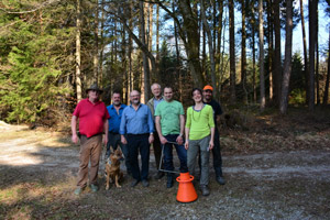 Gruppenfoto mit sechs Männern, einer Frau und einem Schäferhund auf einem Waldweg.