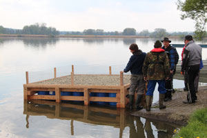 Einige Männer lassen ein Floß ins Wasser eines ruhigen Sees gleiten.