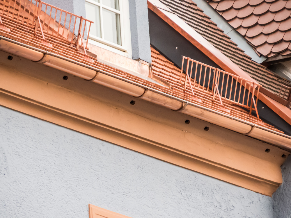 Detailansicht einer frisch renovierten Hausfassade mit Ziegeldach, Schneefang und Dachgauben.