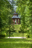 Ein bunt bemalter Pavillon steht auf einem kleinen Hügel inmitten grüner Wiesen und Laubbäume.
