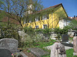 Friedhofsmauer mit Gräbern im Vordergrund und Kirche im Hintergrund.