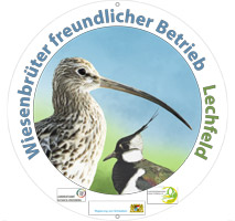 Es ist eine runde Plakette abgebildet. In farbiger Schrift trägt sie die Aufschrift „Wiesenbrüterfreundlicher Betrieb“ sowie den jeweiligen Gebietsnamen. Zentraler Bestandteil der Plakette ist eine Grafik von Kiebitz und Großem Brachvogel. Weiter sind die Logos der Beteiligten Akteure abgebildet; z. B. Landratsämter, Regierung von Schwaben oder die Landschaftspflegeverbände.