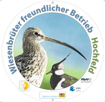 Es ist eine runde Plakette abgebildet. In farbiger Schrift trägt sie die Aufschrift „Wiesenbrüterfreundlicher Betrieb“ sowie den jeweiligen Gebietsnamen. Zentraler Bestandteil der Plakette ist eine Grafik von Kiebitz und Großem Brachvogel. Weiter sind die Logos der Beteiligten Akteure abgebildet; z. B. Landratsämter, Regierung von Schwaben oder die Landschaftspflegeverbände.