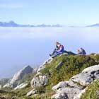 Ein Junge und ein Mädchen sitzen auf einem kleinen Felsen, etwas weiter hinten sitzen zwei Jungen. Die Schüler füllen ihre Forschungsprotokolle in der Sonne über den Hochnebelfeldern aus.