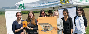 Sechs junge Frauen halten ein Plakat hoch. Im Hintergrund eine Ackerfläche.