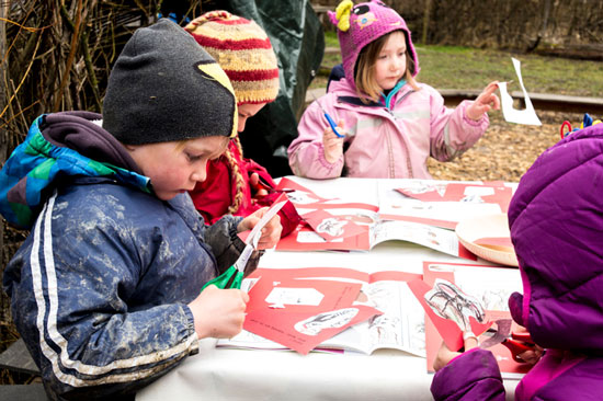 Vier Kinder sitzen am Basteltisch und schneiden im Entdeckerbuch Vorlagen aus.