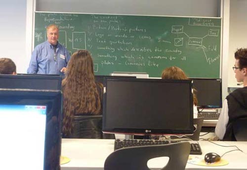 Ein Lehrer steht an der Tafel und erläutert die Gestaltung der Schilder.