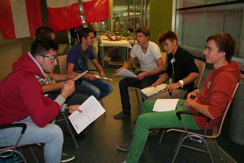 Schüler sitzen im Kreis mit Arbeitsunterlagen auf dem Schoß.