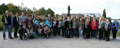 Gruppenbild von Schülerinnen, Schülern, Lehrkräften und ANL-Mitarbeiterinnen auf einem Platz im Pflanzgarten mit Bäumchen in der Hand.