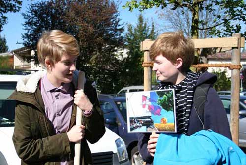 Zwei Schülerinnen zeigen ein Baumschild vor dem gepflanzten Baum.