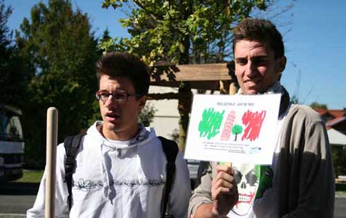 Zwei Schüler zeigen und erläutern ein Baumschild vor dem gepflanzten Baum.