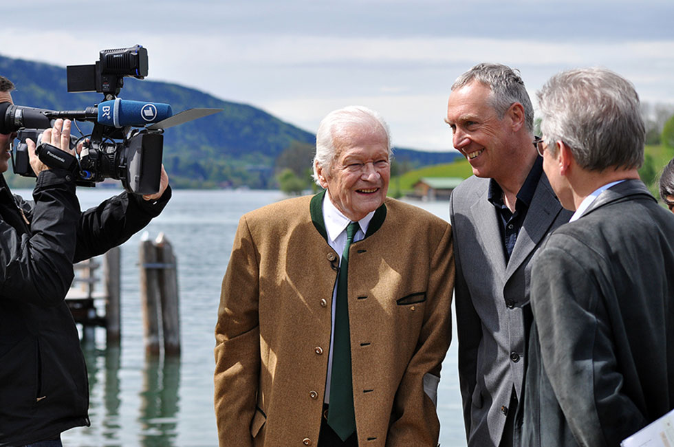 Zwei Herren im Gespräch miteinander werden vor einer Seekulisse von einem Kameramann des Bayerischen Rundfunks gefilmt.