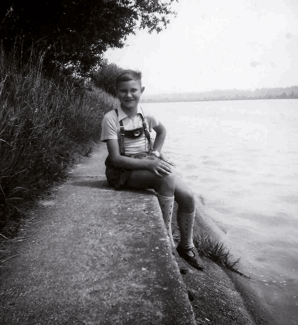 Historisches Foto eines Jungen in Lederhose an einem Flussufer aus den Fünfziger Jahren.