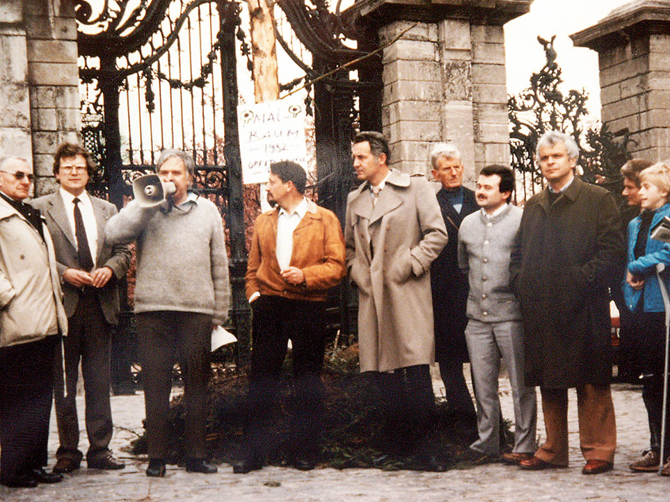 Menschengruppe mit Megafon vor einem Tor in den Achziger Jahren.