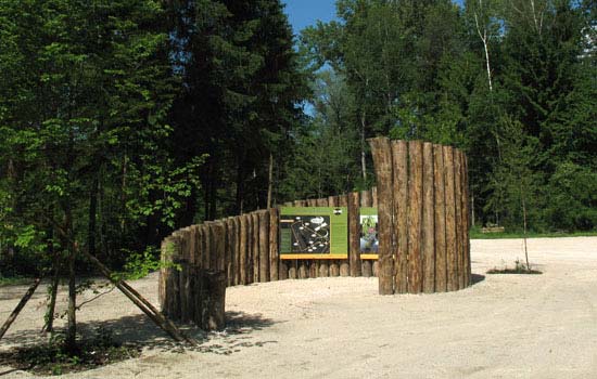 Parkplatz mit Spirale aus stehenden Lärchenstämmen, im Hintergrund Wald