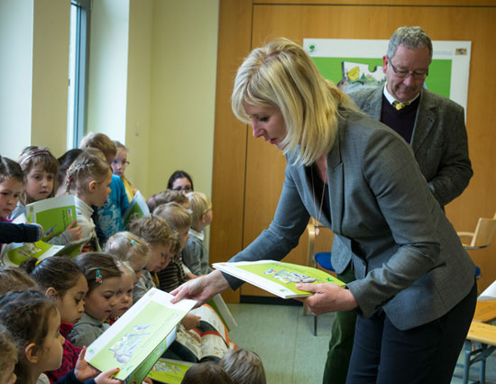 Staatsministerin Ulrike Scharf verteilt das Entdeckerbuch Natur an die Kindergartenkinder. Im Hintergrund steht der Direktor der ANL, Herr Dieter Pasch.