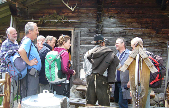 Alte Berghütte vor der sieben Teilnehmende stehen und freundlich begrüßt werden.