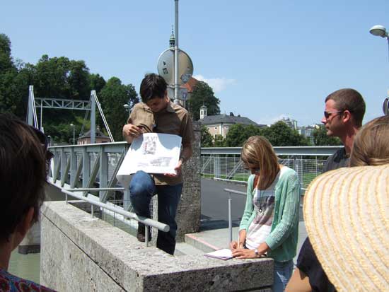 Referent Franz Damm steht mit Konzeptheft am Rande einer Brücke, davor vier Exkursionsteilnehmer.