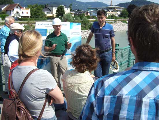 Dr. Thomas Rücker und DI Pfisterer vor einer Infotafel des Kraftwerks Sohlstufe Lehen, im Vordergrund fünf Exkursionsteilnehmer.