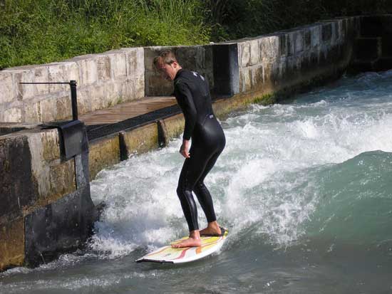 Mann in Neoprenanzug auf einem Surfbrett auf der stehenden Welle reitend.