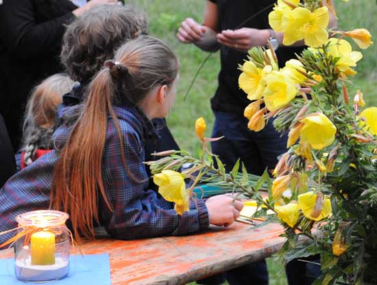 Mehrere Kinder sitzen am Tisch und hören den Ausführungen eines Wissenschaftler zu. Im Vordergrund leuchtendgelbe Nachtkerzen mit geöffneten Blüten.