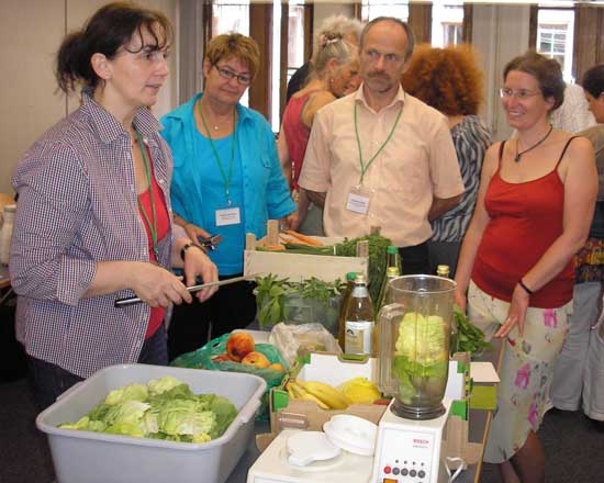 Mehrere Veranstaltungsteilnehmerinnen und -teilnehmer sehen der Kräuterpädagogin bei der Zubereitung von Kopfsalat-Smoothies zu.