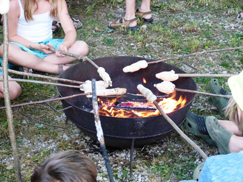 Das von den Kindern aufgespießte Brot wird über dem Lagerfeuer gebacken.