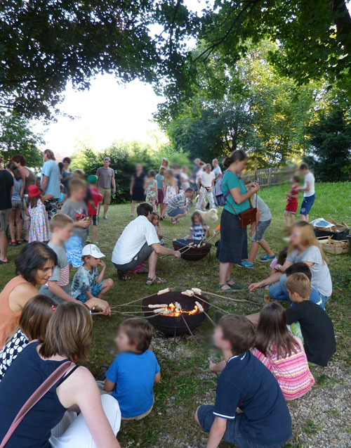 Kinder und Erwachsene sitzen um ein Lagerfeuer und backen Stockbrot.