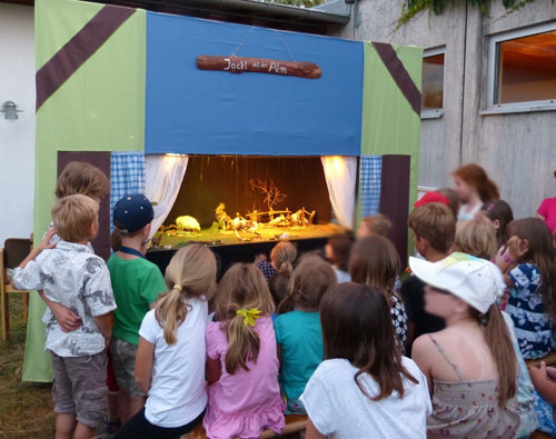 Kinder schauen gebannt auf die aus Naturmaterialien gebaute Kulisse des Marionettentheaters Jockl auf der Alm.